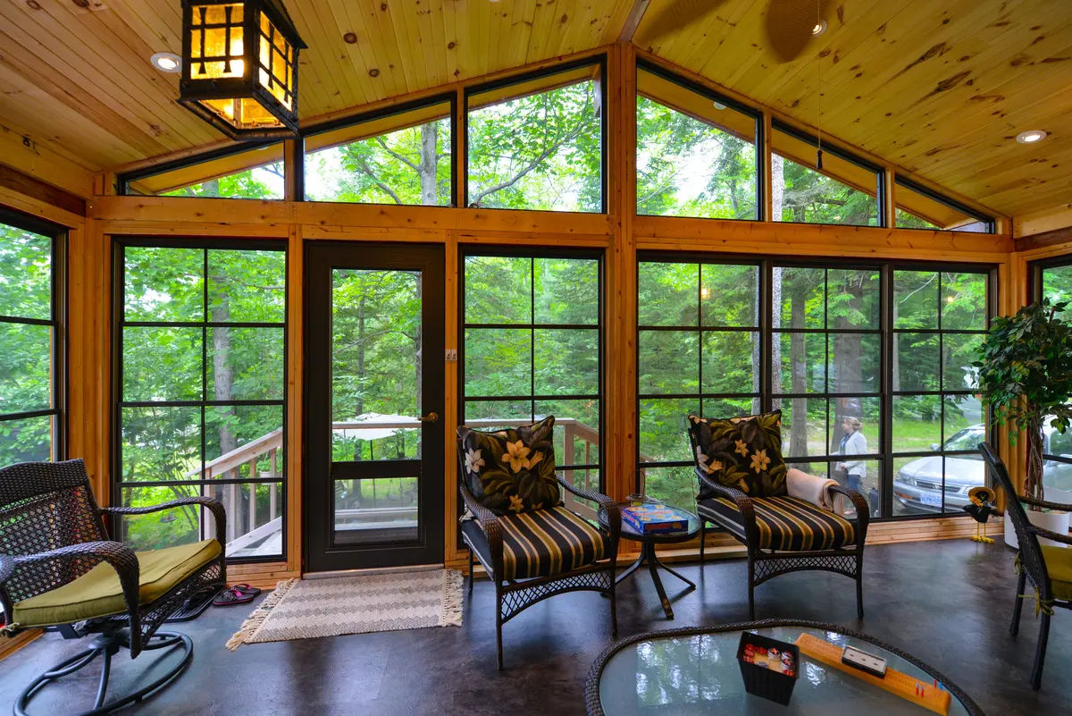 Interior of a sunroom with pine wood walls, featuring large WeatherMaster windows and a matching door overlooking a forest.
