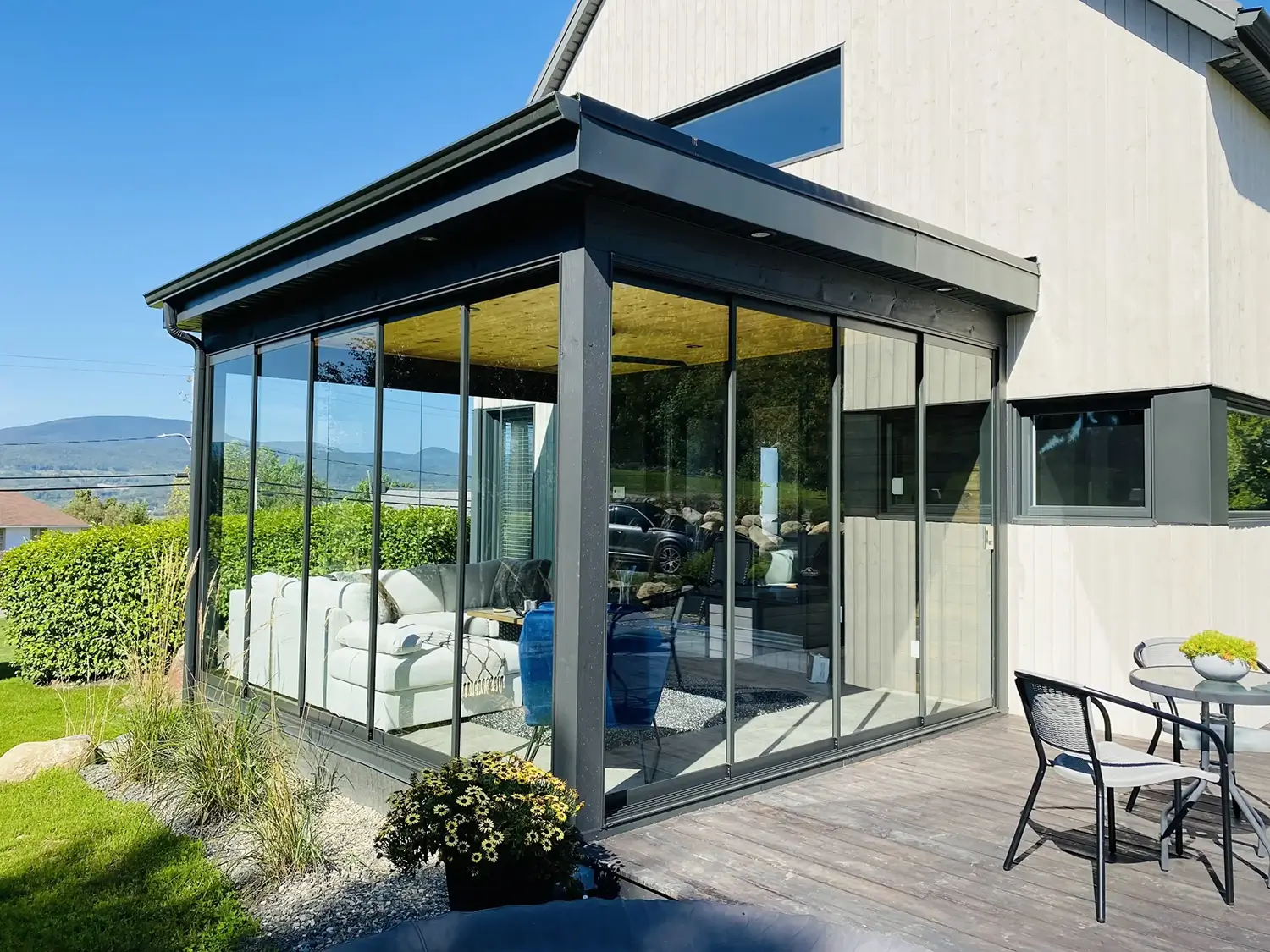 Exterior of a modern NovaSun Horizon Plus sunroom with frameless glass sliding walls and a solid insulated flat roof.