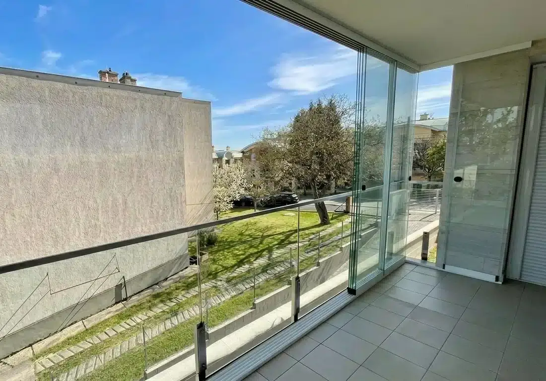 A modern balcony featuring the NovaSun Panoramic frameless sliding glass system with a clear view of a neighborhood.